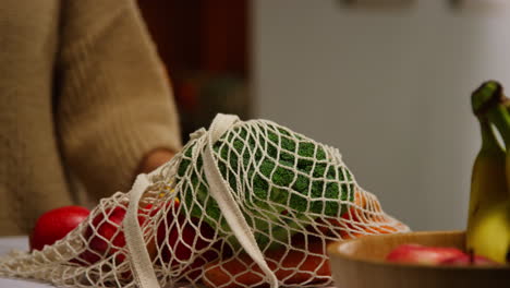 close up of woman unpacking bag of fresh healthy fruit and vegetables onto counter in kitchen 2