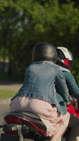two women riding a power bike, with the rider slowing down due to traffic, the rider s button is open, revealing her signet, and her friend holds on from behind, cars can be seen ahead in traffic