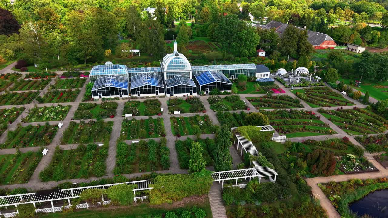Aerial view of Vytautas Magnus University Botanical Garden in Kaunas, Lithuania, showcasing greenhouses, symmetrical garden layouts, and diverse plant collections in a lush natural setting