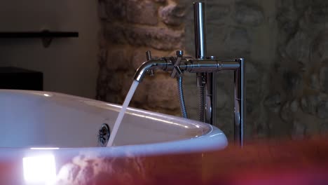 slow motion shot of a bath tap filling the tub in a stone bathroom