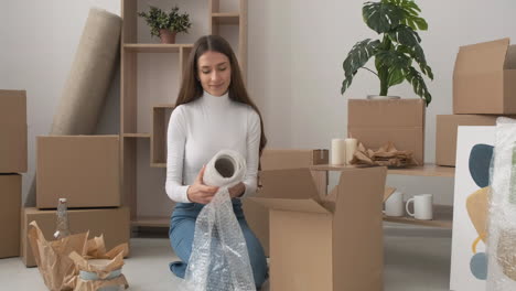 mujer sonriente envolviendo un jarrón con plástico de burbujas y empaquetándolo en una caja de cartón