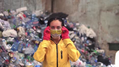 Porträt-Einer-Jungen-Arbeiterin-In-Roten-Gummihandschuhen,-Die-Eine-Maske-Und-Eine-Schutzbrille-Aufsetzen-Und-Sich-Auf-Den-Arbeitstag-Der-Recyclingfabrik-Vorbereiten