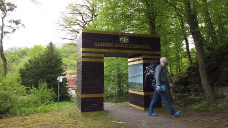 Excursionista-Masculino-Pasando-Por-La-Puerta-Simbólica-En-La-Ciudad-De-Pforzheim-Iniciando-El-Popular-Sendero-De-Larga-Distancia-Westweg-A-Través-Del-Bosque-Negro-En-El-Sur-De-Alemania