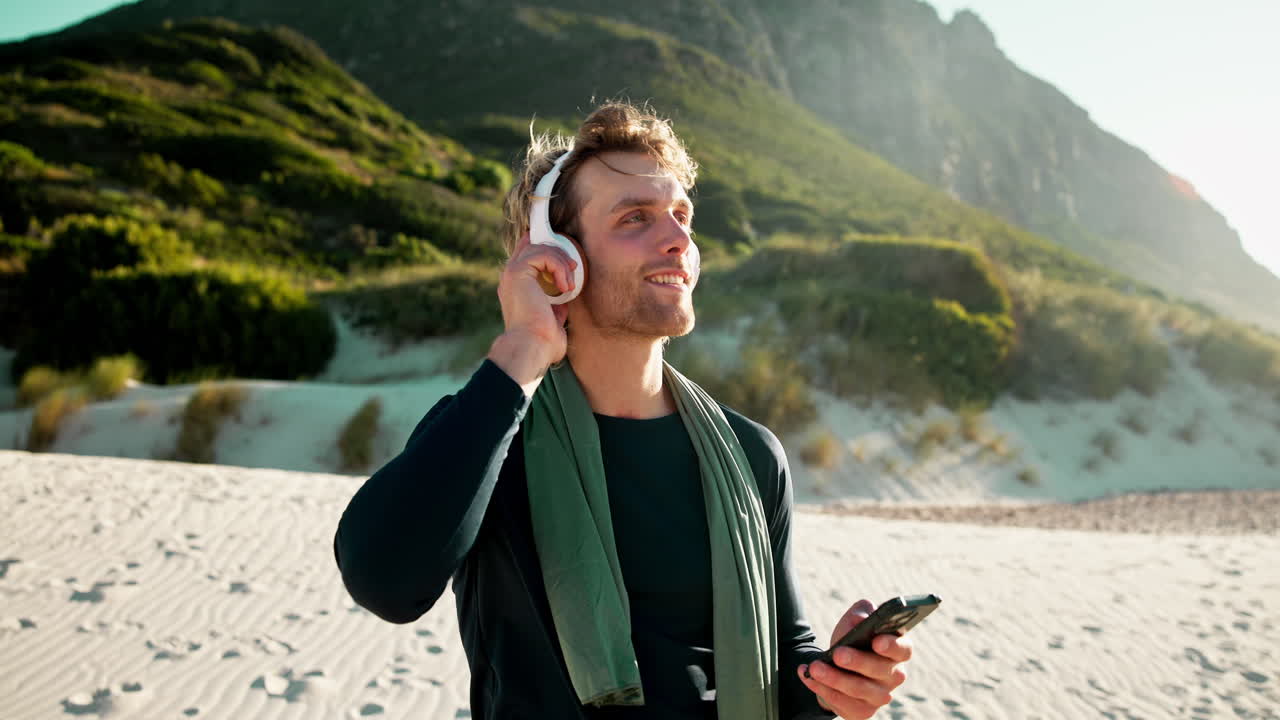 Giovane uomo che ascolta musica con le cuffie su una spiaggia assolata