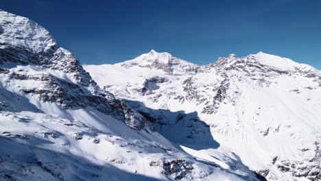 Revelación-Aérea-Del-Paisaje-Montañoso-Cubierto-De-Nieve-Con-Bosques-En-Un-Soleado-Día-De-Invierno-En-Alp-Grum,-Suiza