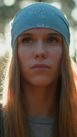 dama con pañuelo azul está de pie en el bosque, profundamente en pensamiento, como la luz del sol crea un resplandor radiante alrededor de su rostro, ella parece tranquila, con su cabello iluminado por el sol filtrando a través de los árboles