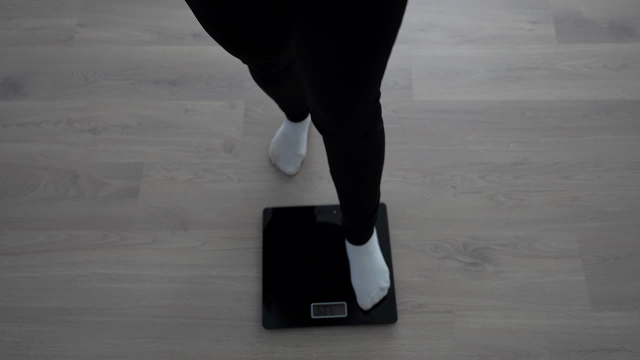 Top down view of pregnant woman stepping on and off digital scale to check weight