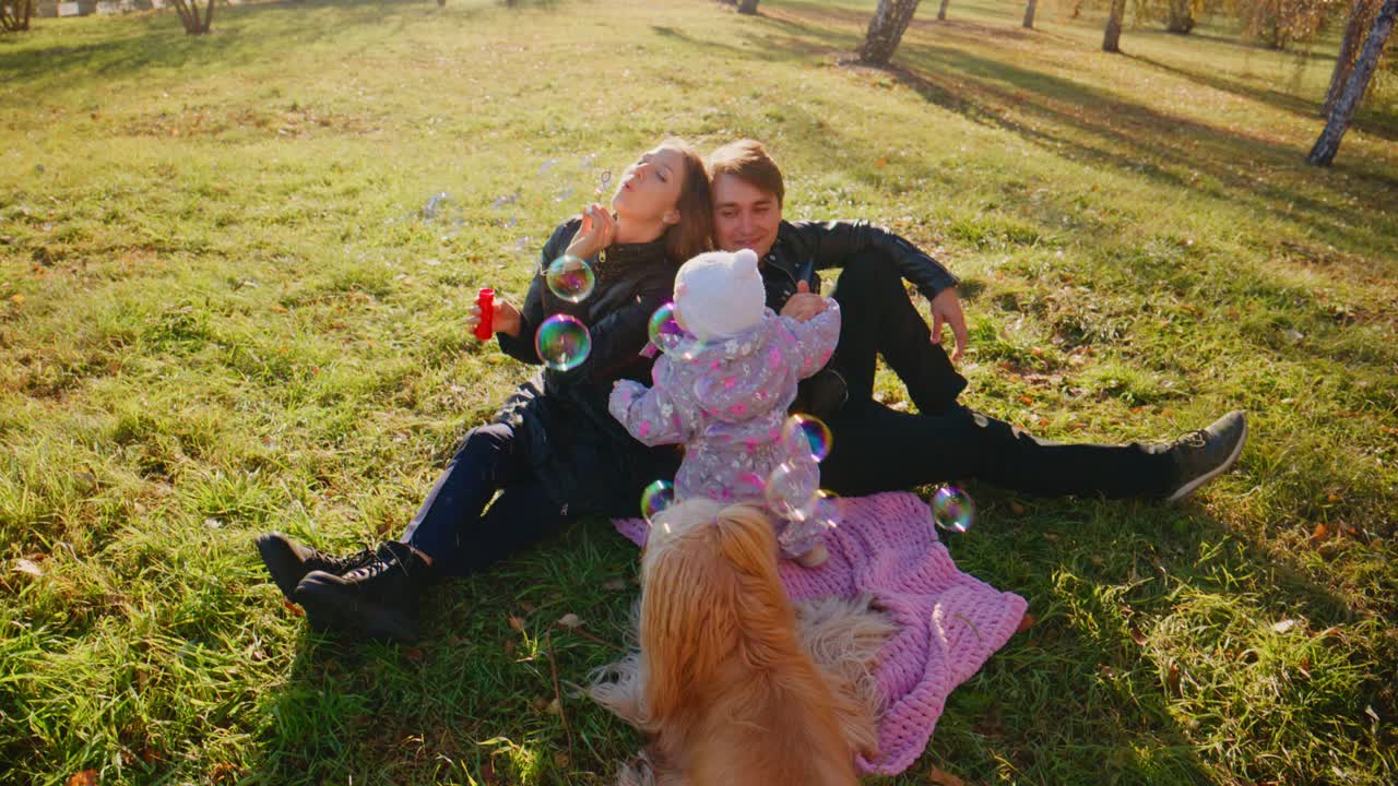 Famiglia che si gode una giornata di relax all'aperto con un cane e un bambino che gioca con le bolle in una calda giornata di sole, circondata dalla natura e da una lussureggiante erba verde