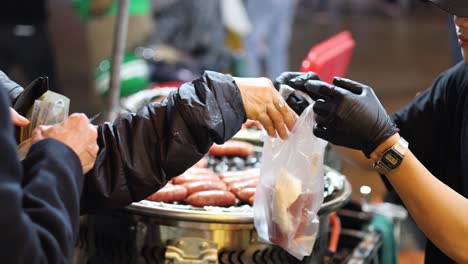 vendor hands over sausages to customers at night