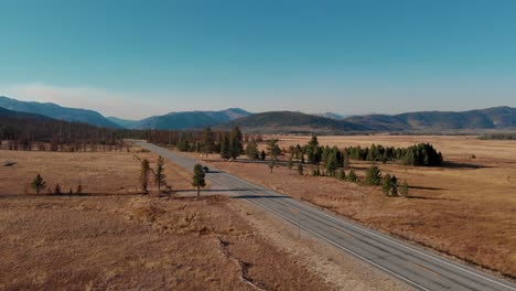 4K-Drohne-Fliegt-über-Offenes-Feld-Und-Auto-Fährt-Die-Landstraße-In-Den-Sawtooth-Mountains,-Stanley,-Idaho-Hinunter