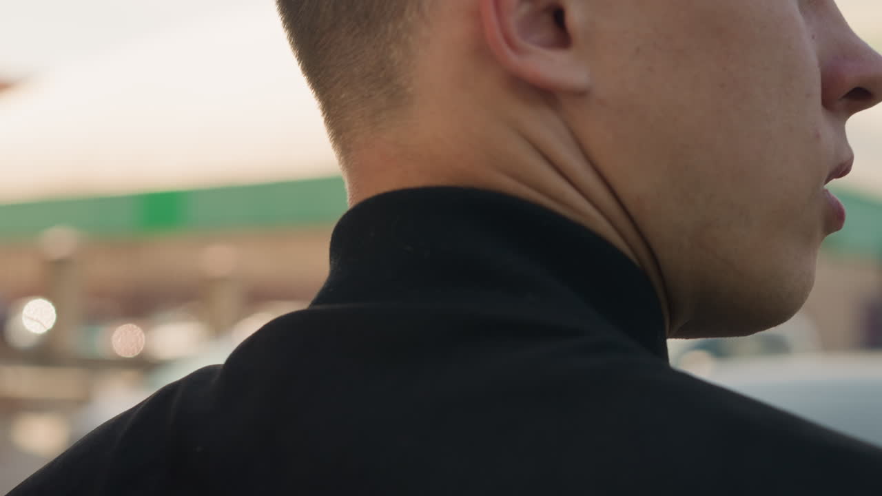 차량 옆에서 옷깃을 정리하는 사람, 주행을 시작하기 전에 주유소에서 옷을 준비하는 남성, 출발하기 전에 길가 주유소에서 차 옆에서 옷을 매무새하는 사람을 돕는 개인