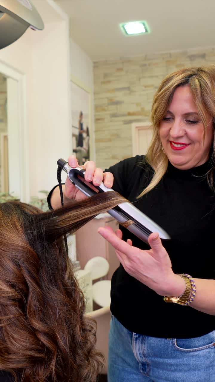 Hairdresser Styling Client's Long Brown Hair with a Flat Iron in a Salon