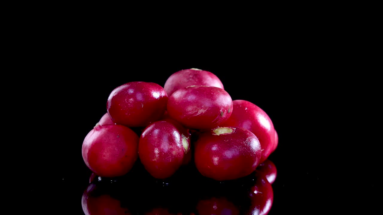 A cluster of radishes rotates on a reflective black surface, highlighting their vibrant color and texture under bright lighting