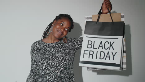 feliz mujer afroamericana posando con bolsas de compras y teléfono inteligente