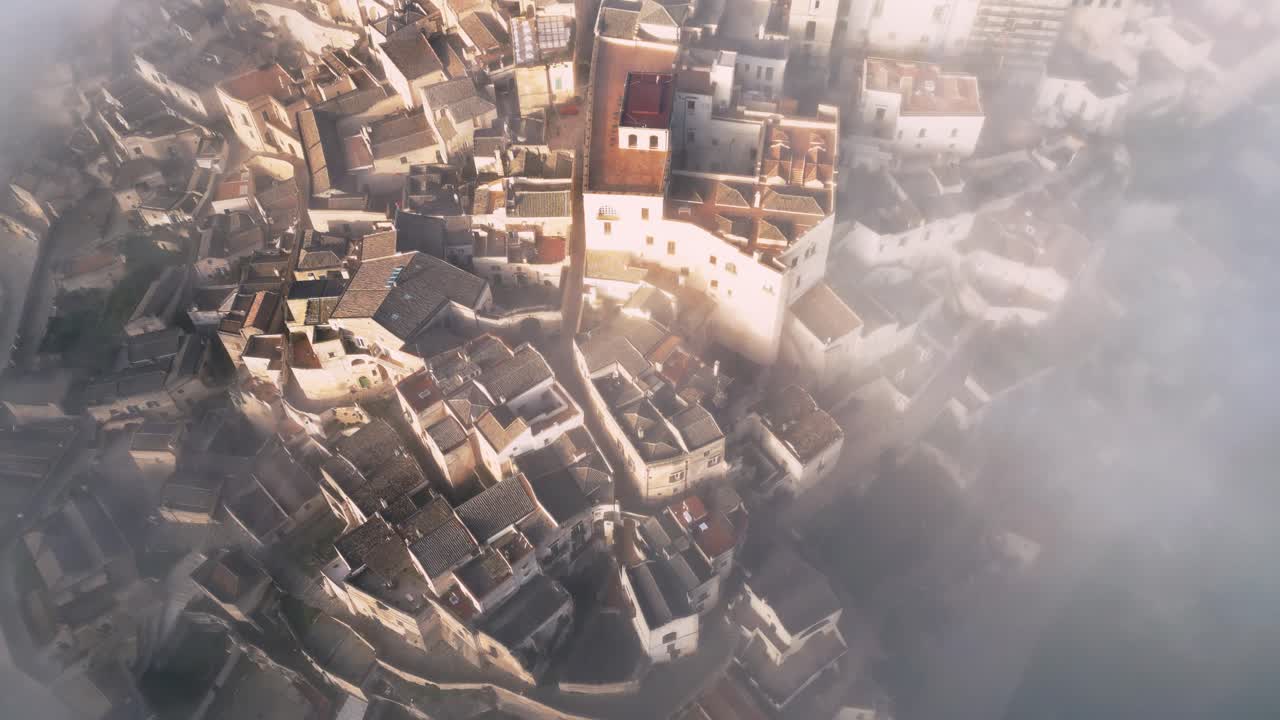 drone shot of old Italian city town - Matera. The city is shrouded with low handing clouds, buildings are visible through them. Warm colours of the rising sun reflected against buildings