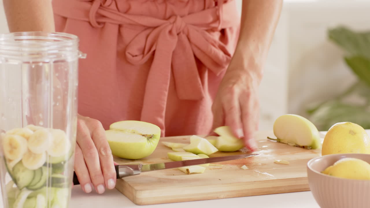Donna che prepara un frullato di frutta fresca con mele e banane in cucina.