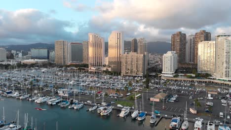 aerial pan over boat harbor, kahanamoku beach lagoon, waikiki beach and honolulu at golden hour, with skyscrapers in the background
