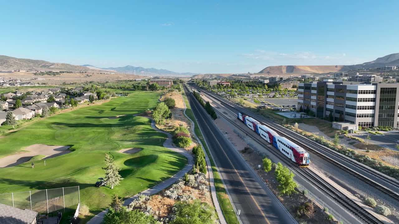 FrontRunner light rail commuter train leaving Lehi Station in Utah Valley towards Provo - pullback aerial follow on a sunny morning