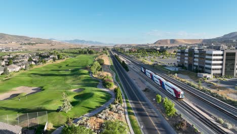 frontrunner light rail commuter train leaving lehi station in utah valley towards provo - pullback aerial follow on a sunny morning