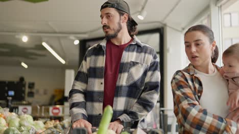 un hombre moreno confiado con una barba junto con su esposa y un niño pequeño con un carrito eligen productos y hacen sus compras en el supermercado