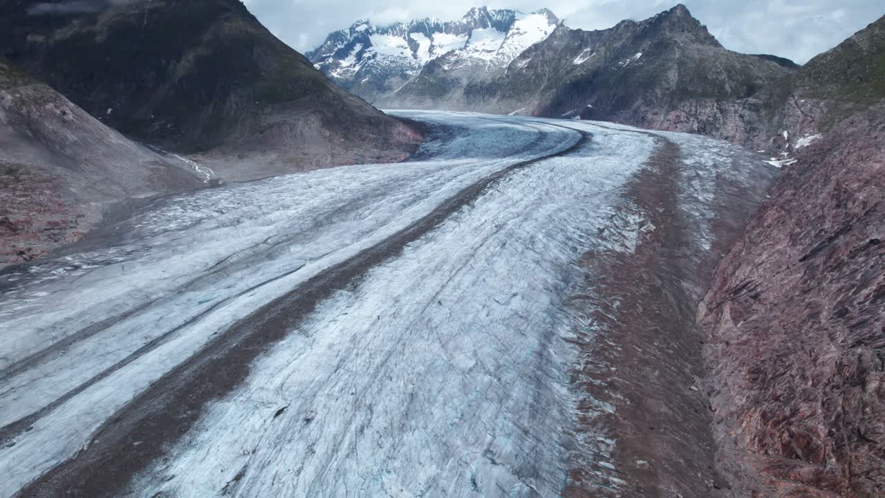 Reverse pullback 4k drone shot revealing the vast Aletsch Glacier stretching through the alpine valley, icy textures and dark moraines unfolding as towering peaks emerge in the distance