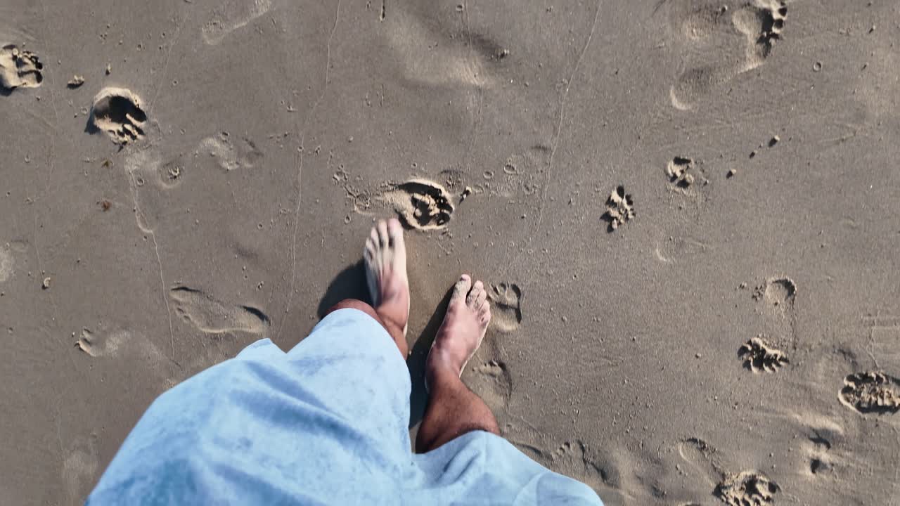 Pov of tourist walking barefoot on wet sandy beach leaving footprints. slow motion