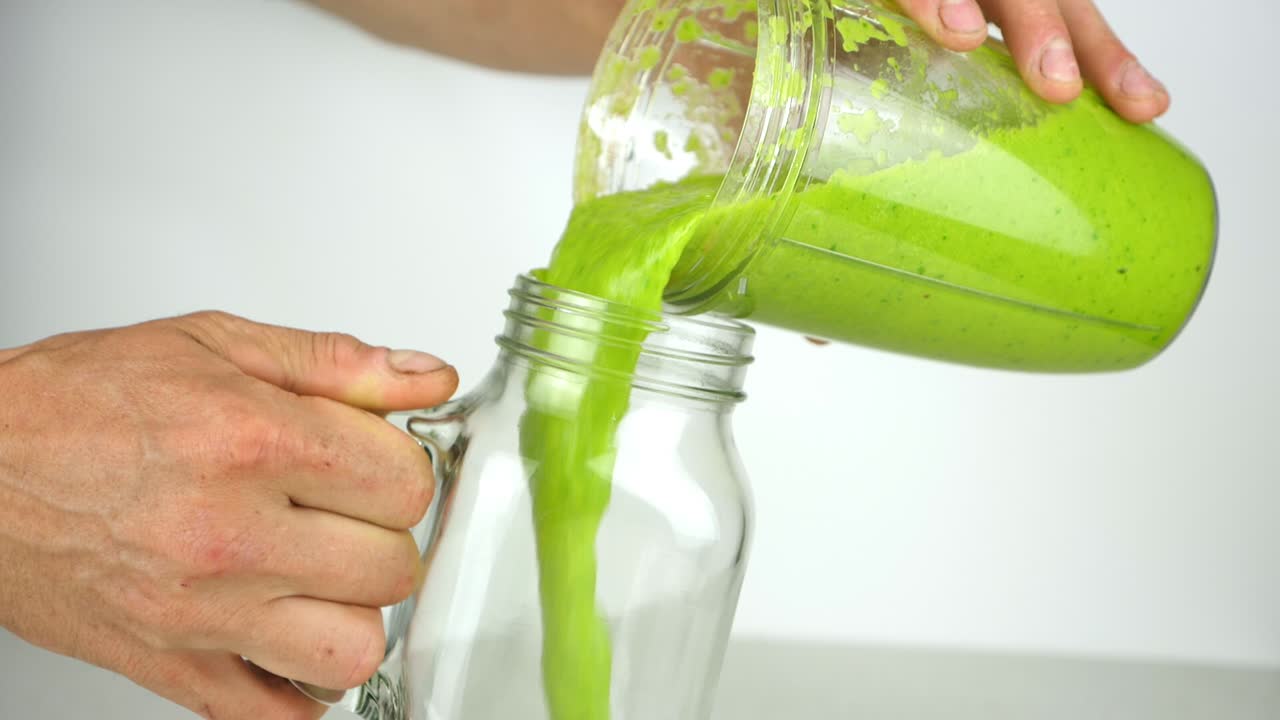 verter un batido verde nutritivo en un divertido tarro de albañil