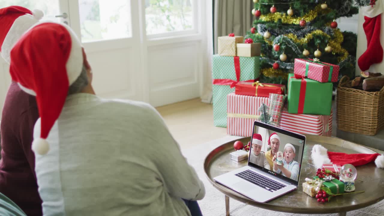amigas mayores diversas usando una computadora portátil para una videollamada de navidad con una familia sonriente en la pantalla