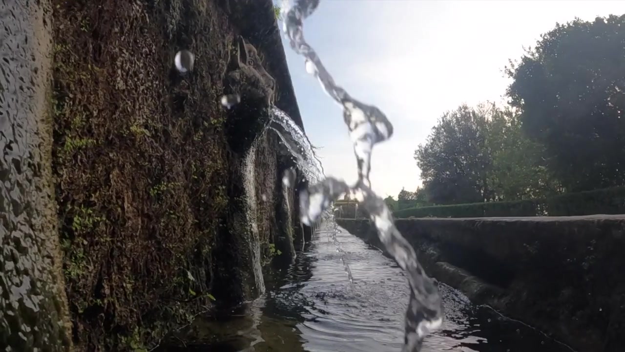 Inquadratura frontale dal basso di acqua che scorre da un muro di pietra muschioso in uno stretto canale da giardino