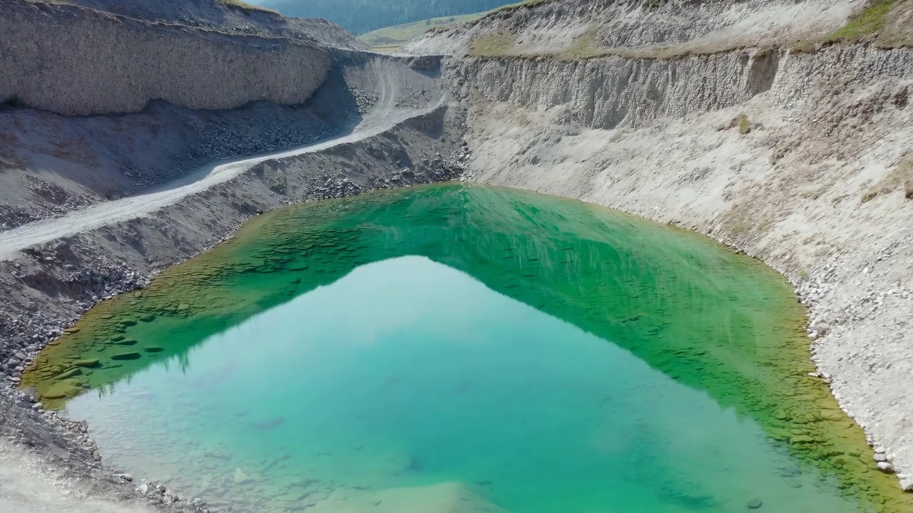 Flygfoto med drönare över turkos kratersjö. Branta bleka klippväggar omger livfullt turkosblått, mineralrikt vatten