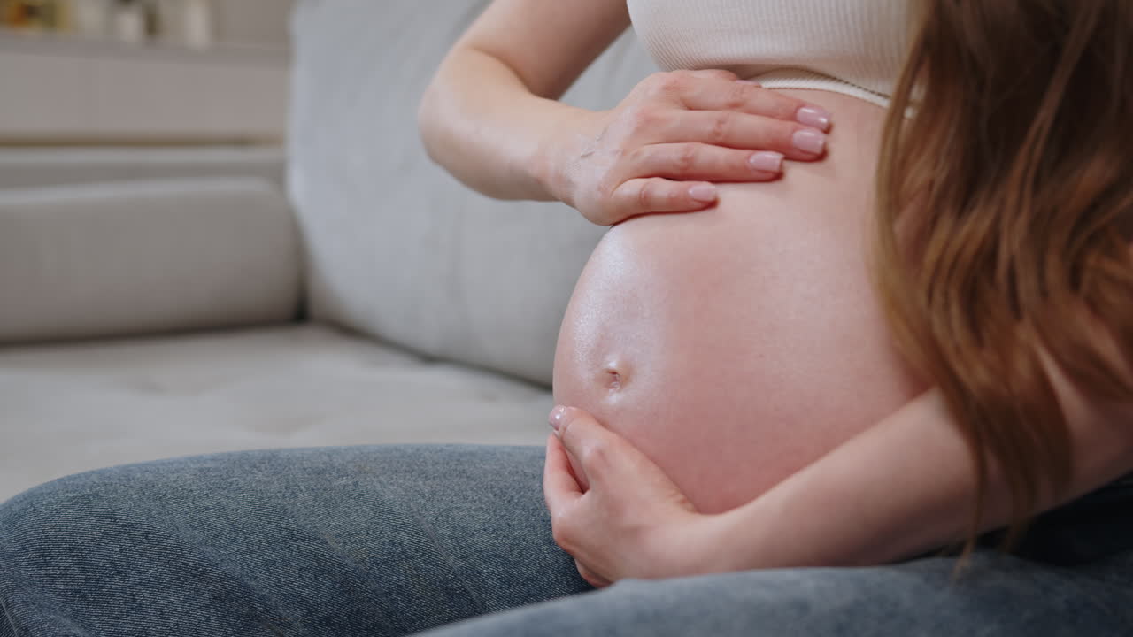 Mani di donna che accarezzano delicatamente il ventre mentre è seduta su un divano, mostrando trepidazione e