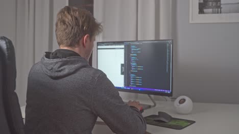 un joven se sienta en el escritorio de su oficina en casa e inmediatamente comienza a editar el código fuente en su computadora para avanzar en su carrera en el desarrollo de software