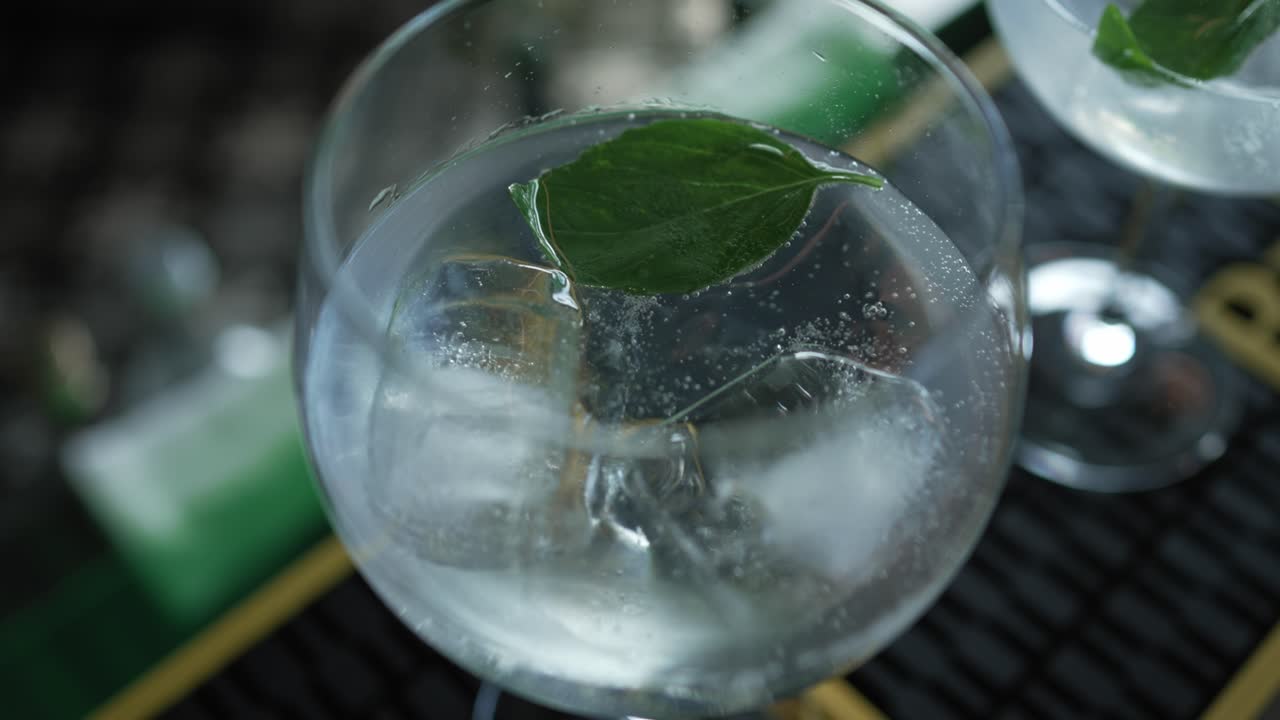 close up of drink being poured over ice and mint leaves in chilled cocktail glass