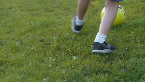 child feet running and kicking football soccer ball. tracking in slow motion