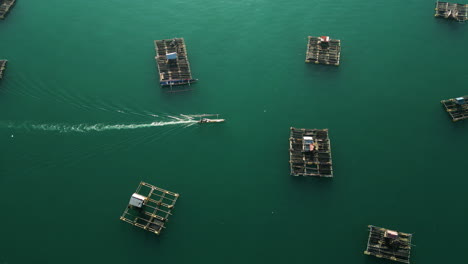 vista aérea de un barco de pesca que navega a través de granjas de peces flotantes en el área de la bahía de tanjung aan, isla de lombok, indonesia