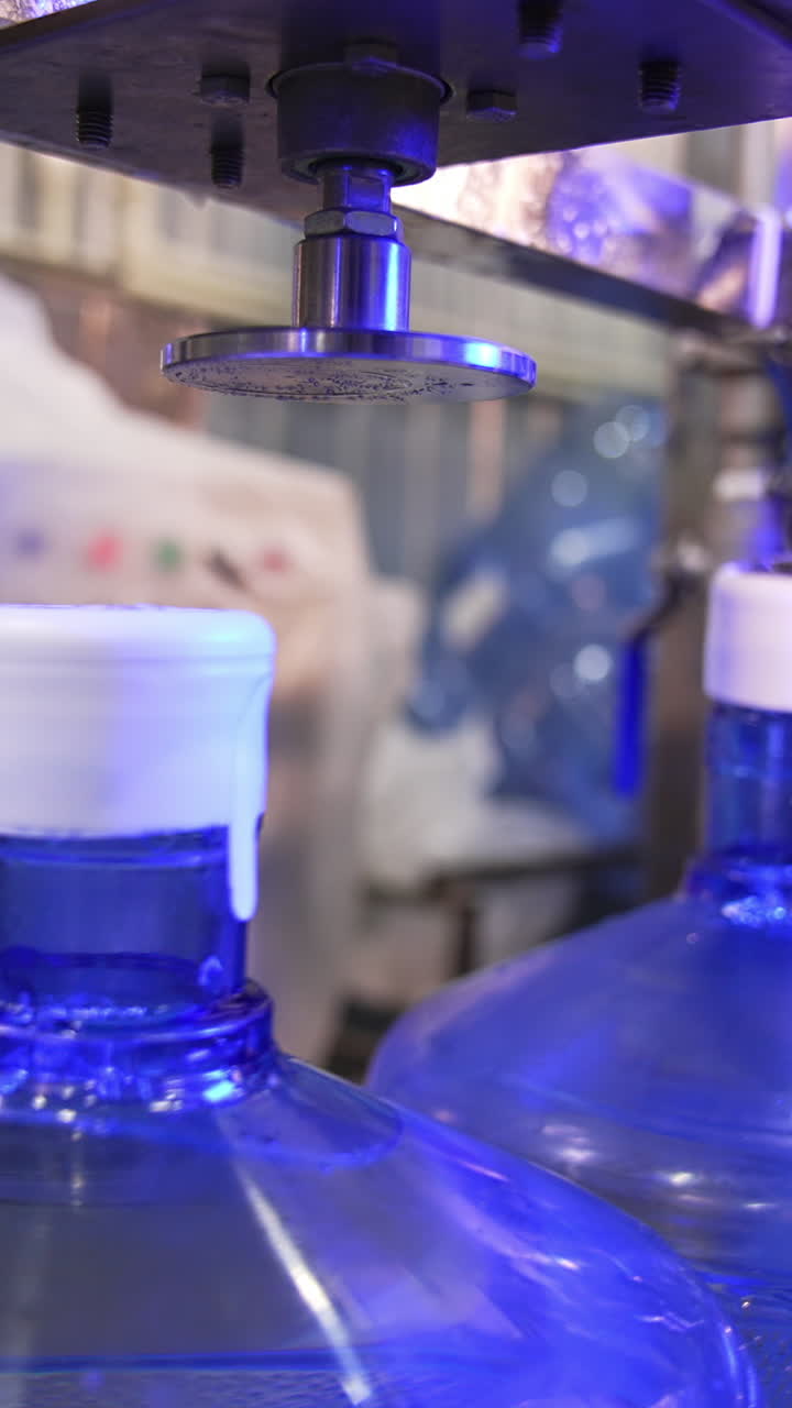 Corking the bottles of fresh clean water. Big flasks filled with water move by the conveyor belt. Mineral water production at factory. Vertical video