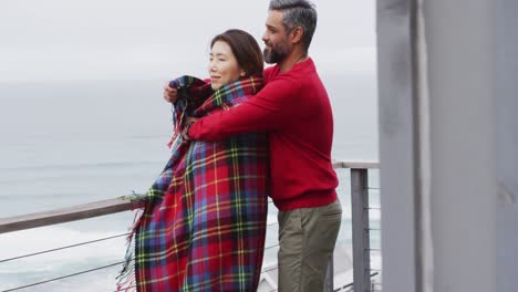 una pareja feliz con una manta abrazándose y hablando juntos en el balcón