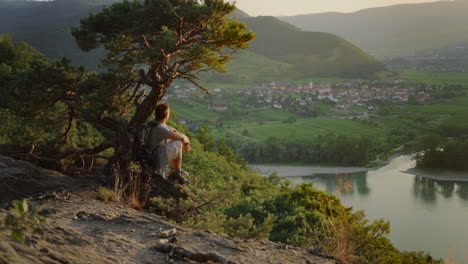 male looking at the golden hour sunset under a tree, mountain landscape background, river danube valley, overview, looking out, peaceful digital detox, outdoor nature, overstimulation detox, travel