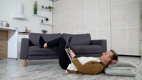 remote job. tired freelancer works on a laptop while lying on the floor in the kitchen. young man studying through the laptop at home. distance education.