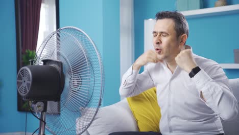 man trying to cool off with fan at home.