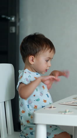small kid looks at puzzles on the table in front of him. lovely baby boy waves his hands excitedly. vertical video