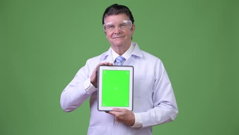 senior handsome man doctor with protective glasses showing digital tablet