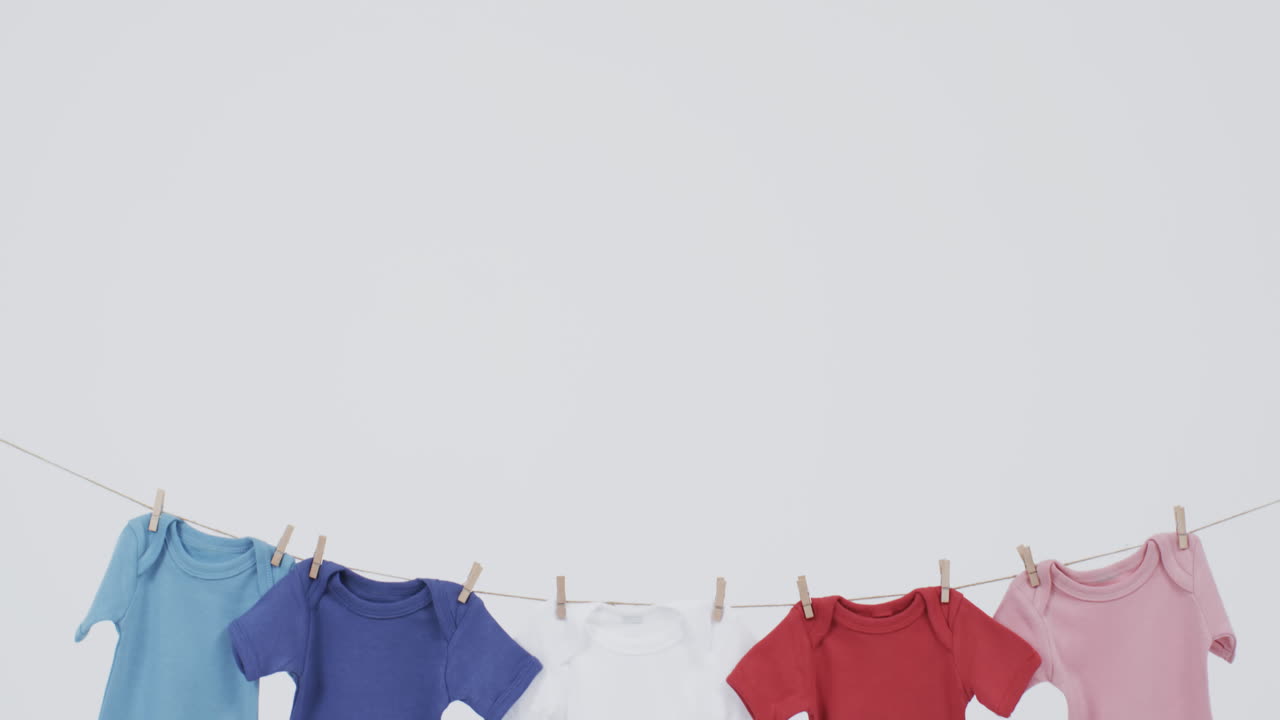Video of multi coloured baby grows hanging on pegs from line with copy space on white background