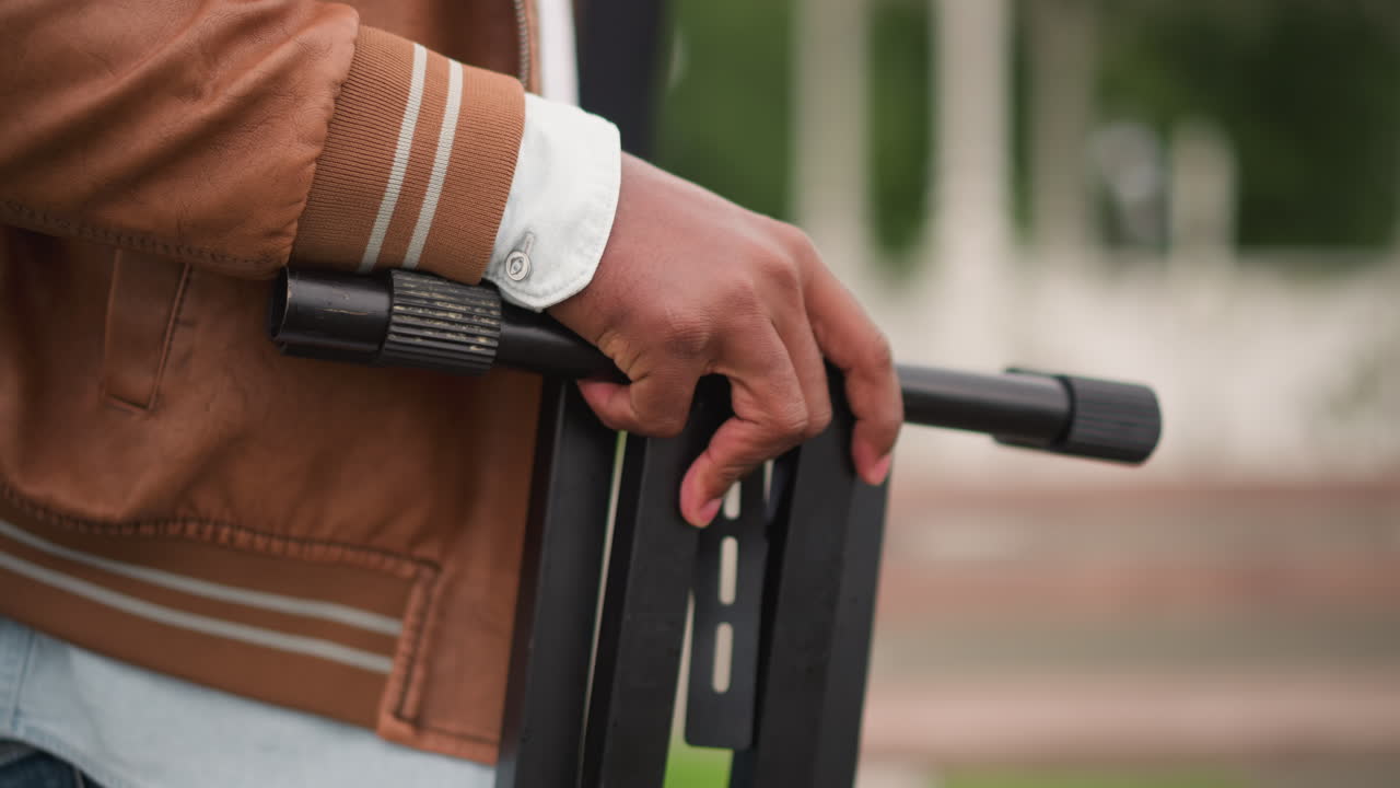 person holding electric scooter handlebar, brown leather jacket, closeup of hands on grip, urban park background, relaxed commuter waiting, shallow depth of field, sustainable mobility, morning