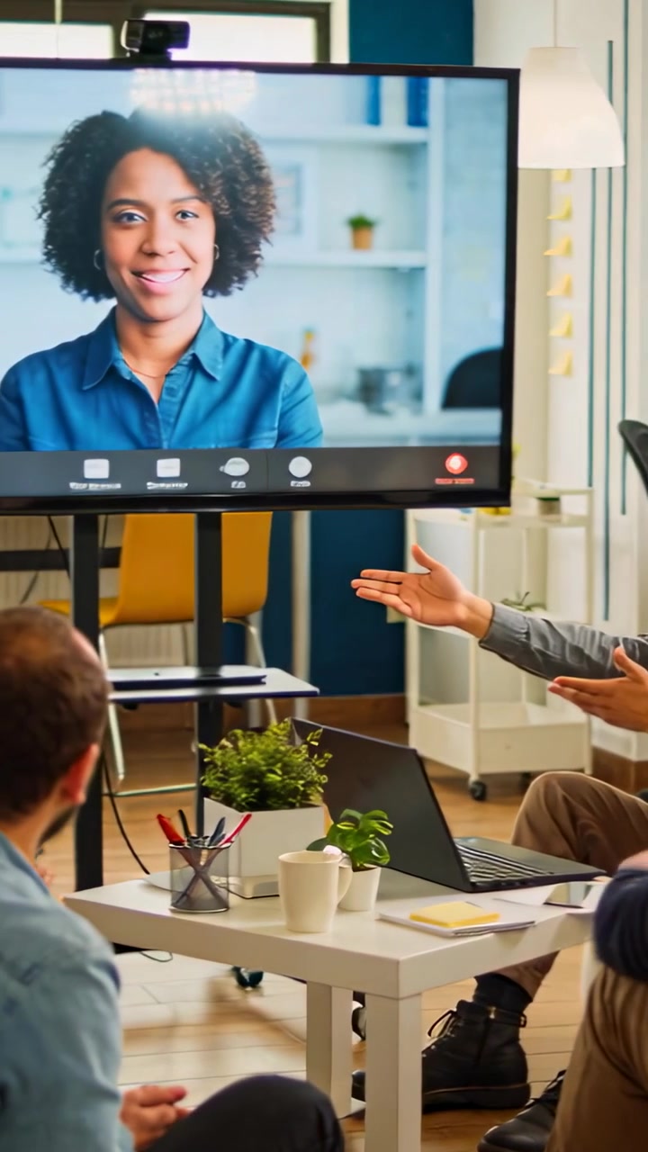 Vertical video: Call starting with remote woman in blue shirt speaking on monitor for team meeting