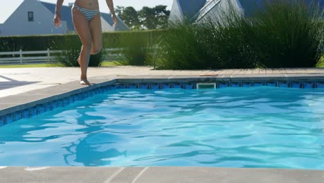 Front-view-of-young-mixed-race-woman-jumping-in-swimming-pool-on-a-sunny-day-4k