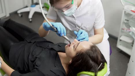 young female dentist in gloves and mask drilling patient's teeth in clinic