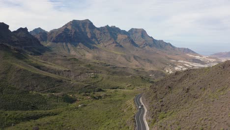 Panorama-drone-shot-of-a-car-driving-through-a-canyon-with-mountains