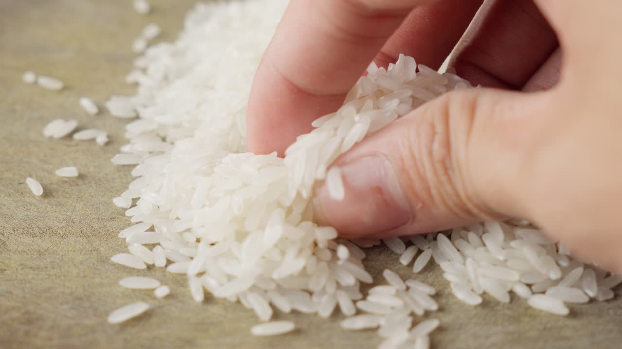 Mano che tocca delicatamente e seleziona chicchi di riso bianco su una superficie piana, primo piano.