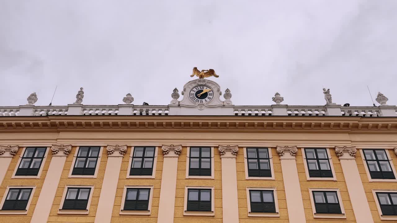 Ornate yellow facade with a decorative clock and statues on top in Vienna, Austria